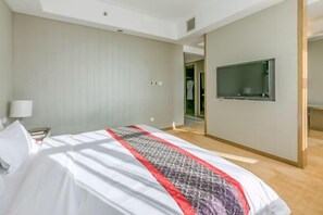 Habitación de hotel con una cama, un televisor montado en la pared y una puerta que da a un baño.
