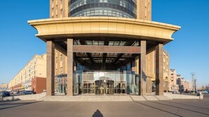 Un bâtiment moderne doté d’une entrée incurvée, de grandes portes vitrées et surplombant un ciel dégagé.