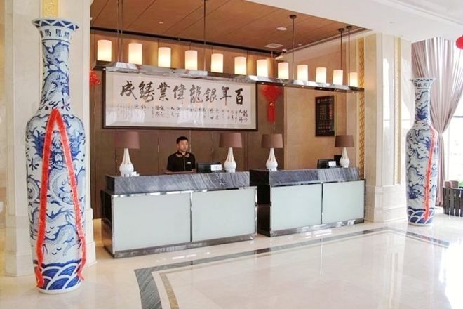 A hotel reception area with a receptionist behind a marble counter, large vases, and a banner with text.