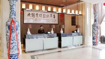 A hotel reception area with a receptionist behind a marble counter, large vases, and a banner with text.