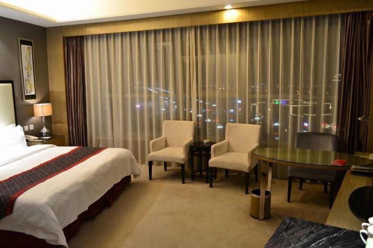 A hotel room with a bed, two armchairs, a glass table, and a view of the city at night.