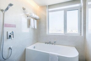 A modern bathroom with a bathtub, a showerhead, and a window with a city view.