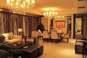 A hotel room with a living area, dining table, and chairs, a chandelier, and a large window with curtains.