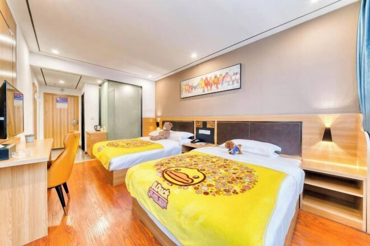 Habitación de hotel con dos camas, un escritorio y una silla. Se observa un cuadro en la pared y un televisor sobre el escritorio.