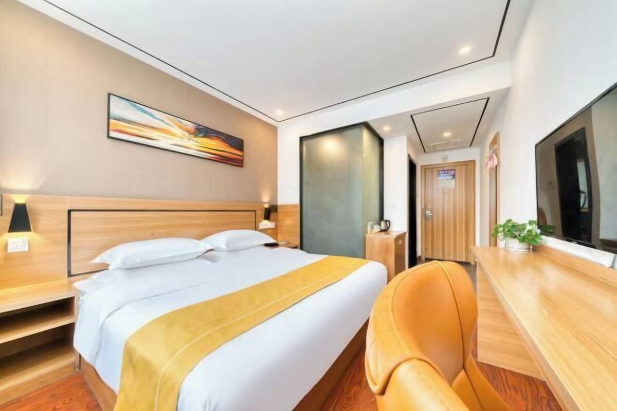 Una habitación de hotel moderna con una cama grande, un escritorio de madera, una silla, un televisor y un cuadro en la pared.