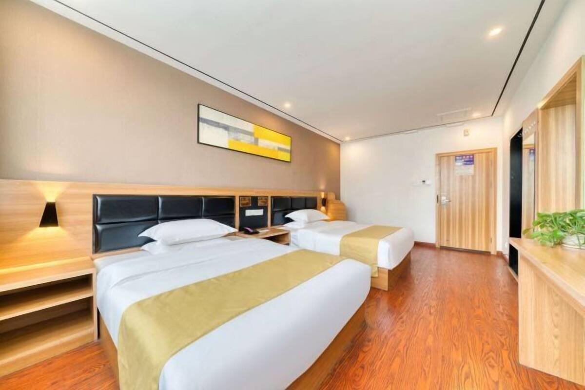 Habitación de hotel con dos camas, suelo de madera, cabecera con lámpara y escritorio de madera con una planta.