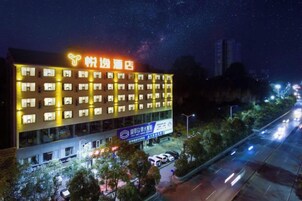 Un hotel de varios pisos con señalización iluminada, estacionamiento y vista a la calle.