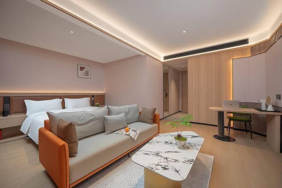 Una habitación de hotel moderna con un sofá, una mesa de comedor, una planta pequeña y una computadora portátil.