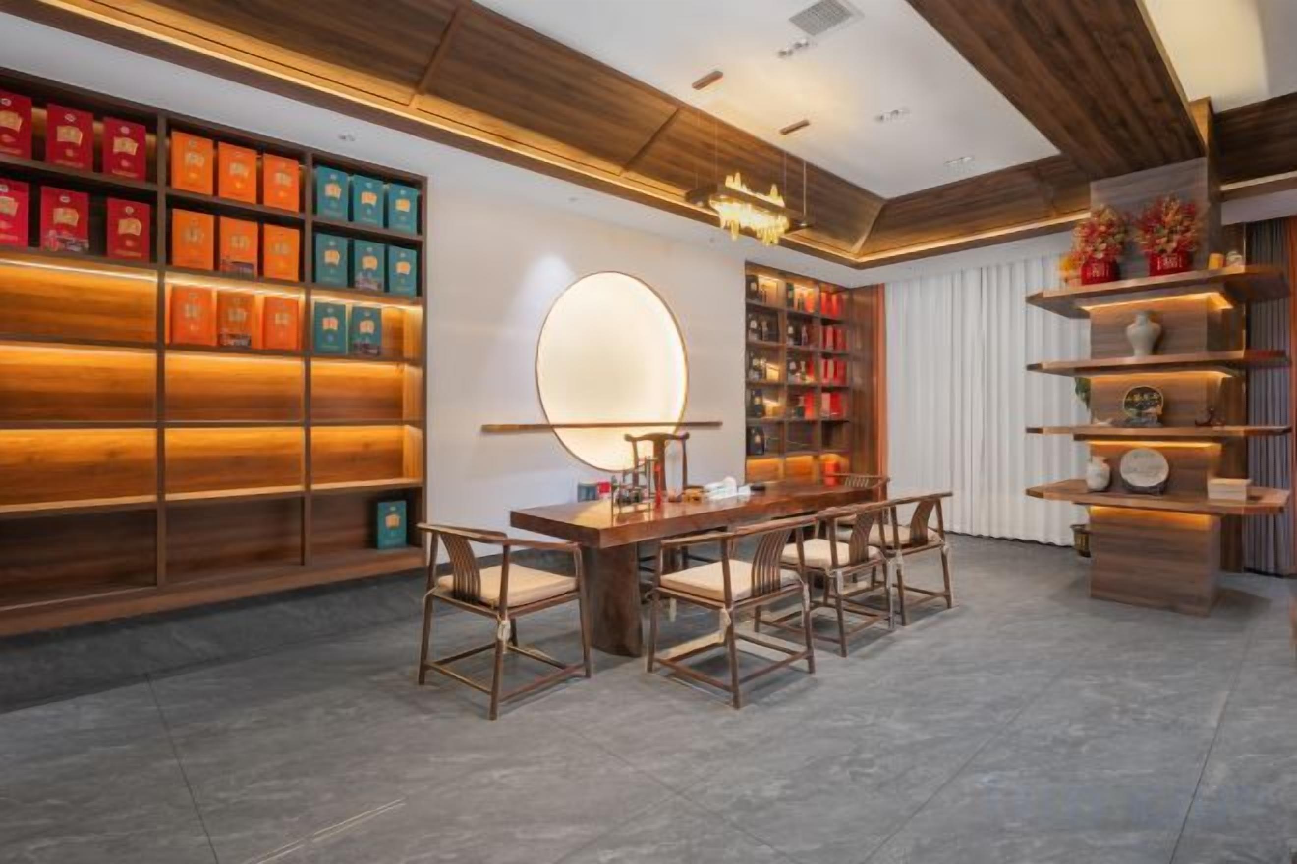 A modern interior with a wooden ceiling, a round mirror, a dining table with chairs, and shelves with books and decorative items.