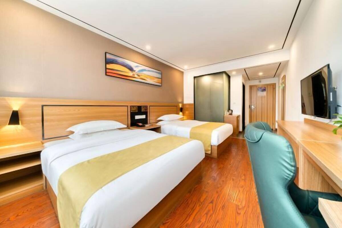 Una habitación de hotel con dos camas, un escritorio, una silla, un televisor y un cuadro en la pared.