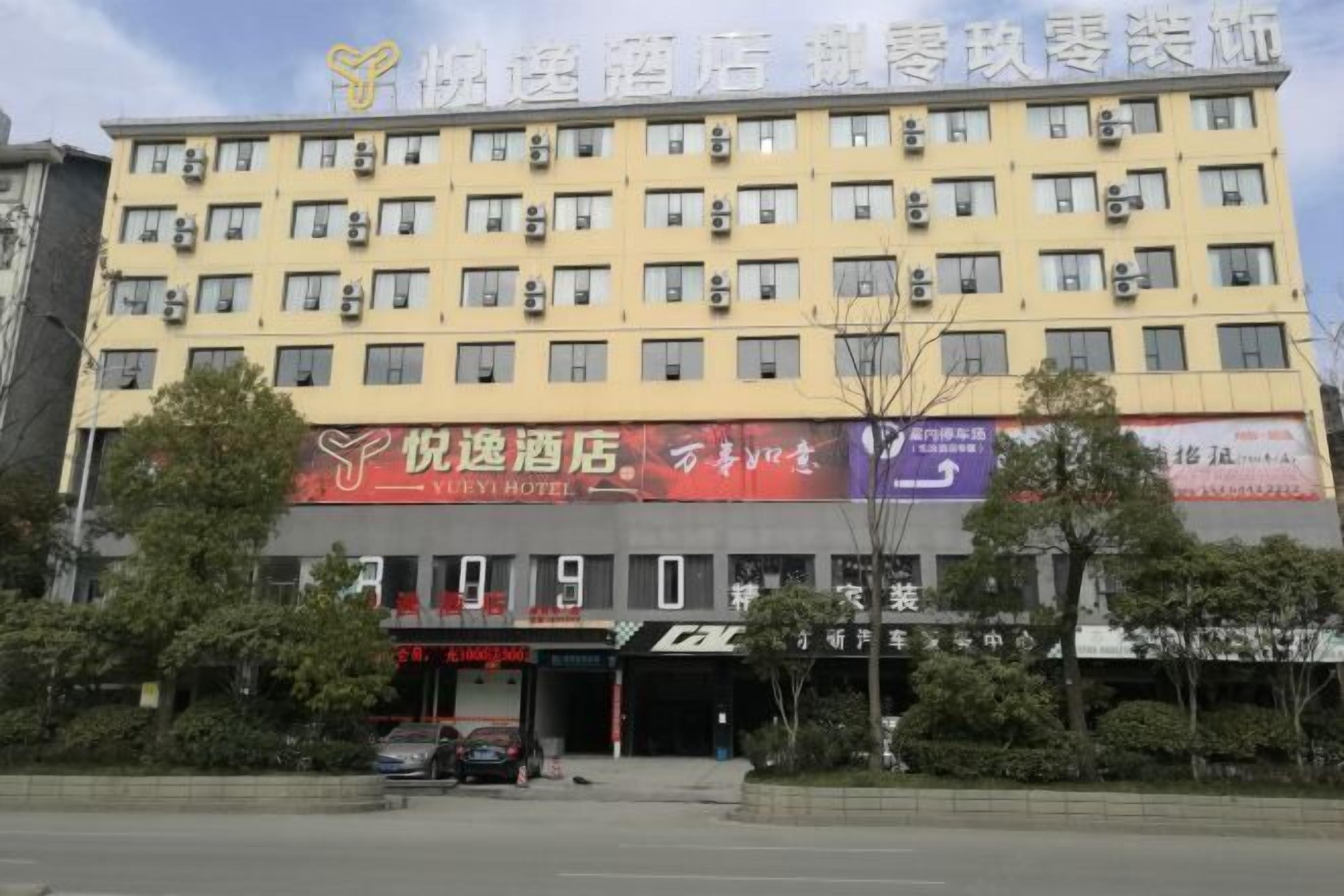A multi-story hotel with a yellow facade, multiple air conditioning units, and several ground-level businesses.