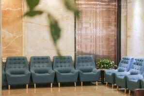 A waiting area with four blue chairs, a small table with a plant, and a marble wall. - Diannan Hotel (Tonghai)