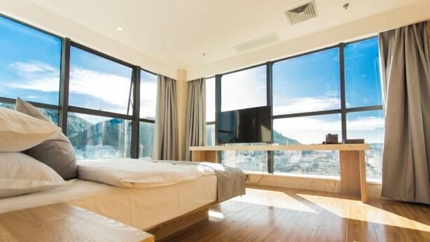 Quarto de hotel moderno com uma cama grande, uma mesa de cabeceira de madeira, televisão de tela plana e grandes janelas com vista para as montanhas.