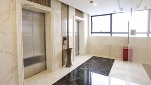 Área de elevador moderna com paredes de mármore e piso preto brilhante.