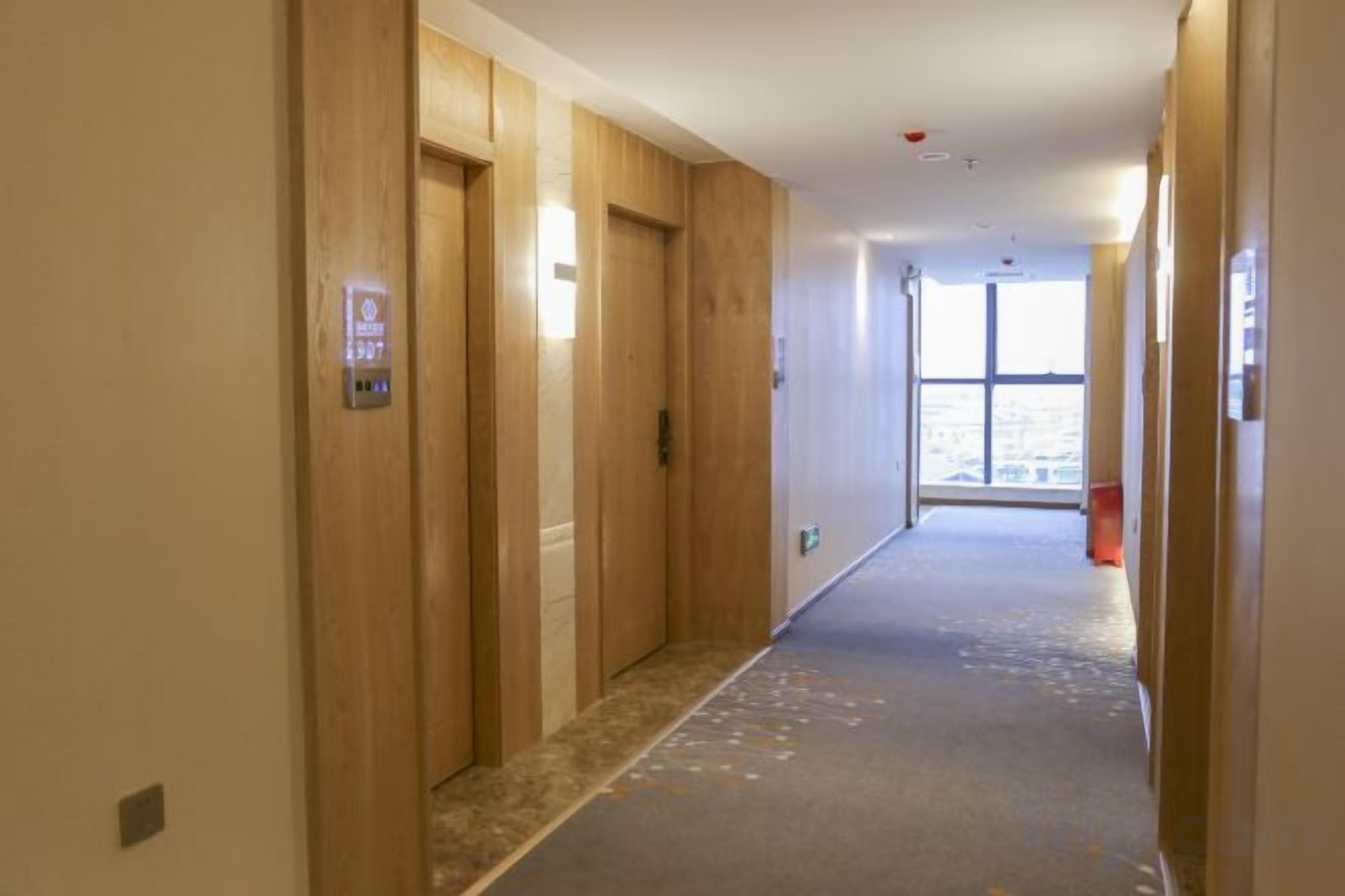Un pasillo con puertas de madera, suelo alfombrado y vistas a través de un ventanal.