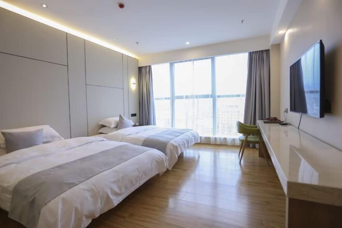 A modern hotel room with two beds, a desk, and a large window with curtains.