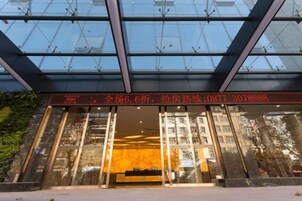 A hotel entrance with a glass facade, a red sign with contact information, and a reflection of trees.