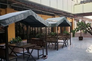 Un espacio al aire libre con techo, mesas y bancos, sombrillas y plantas en macetas.