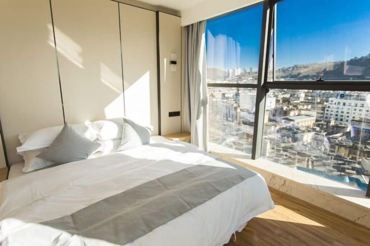 A modern hotel room with a large bed, a city view through floor-to-ceiling windows, and a minimalist design.