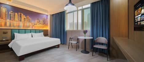 A hotel room with a bed, a small table with chairs, a cityscape mural, and a large window with curtains.