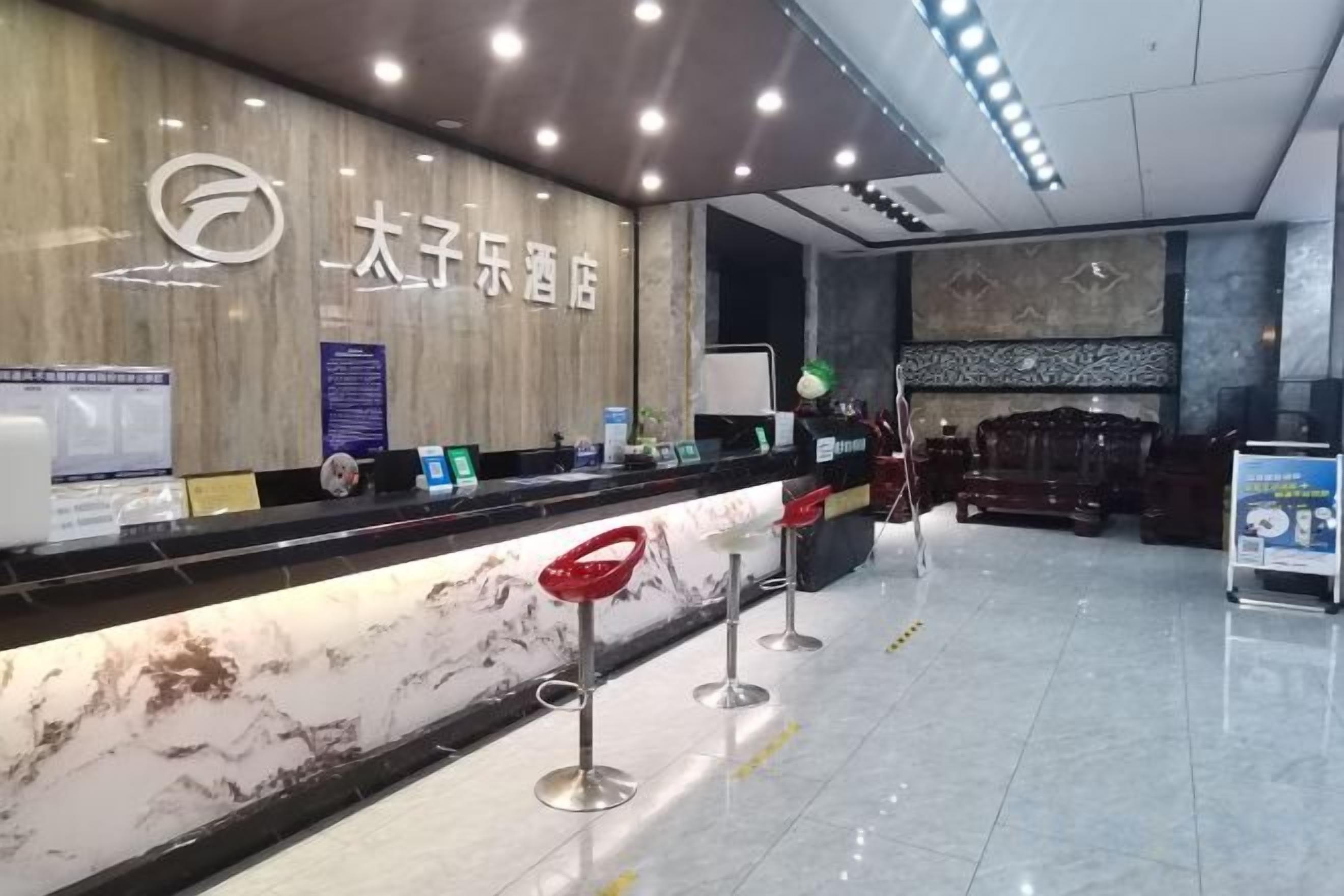Zona de recepción de un hotel con mostrador de mármol, taburetes rojos y un letrero.