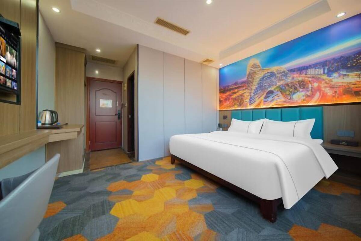 A hotel room with a large bed, a painting on the wall, and a view of the cityscape.