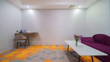 Una habitación con escritorio, silla, sofá morado y una mesa con un jarrón de flores.