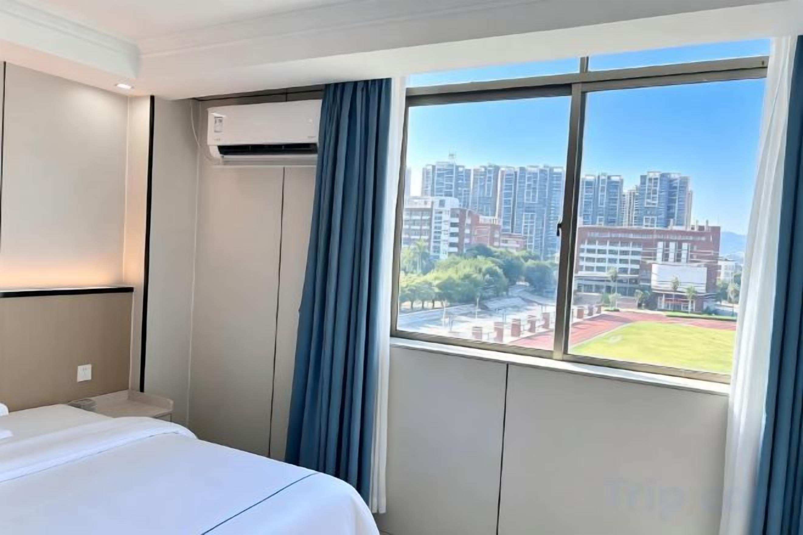 A hotel room with a bed, air conditioning unit, and a window with a city view.