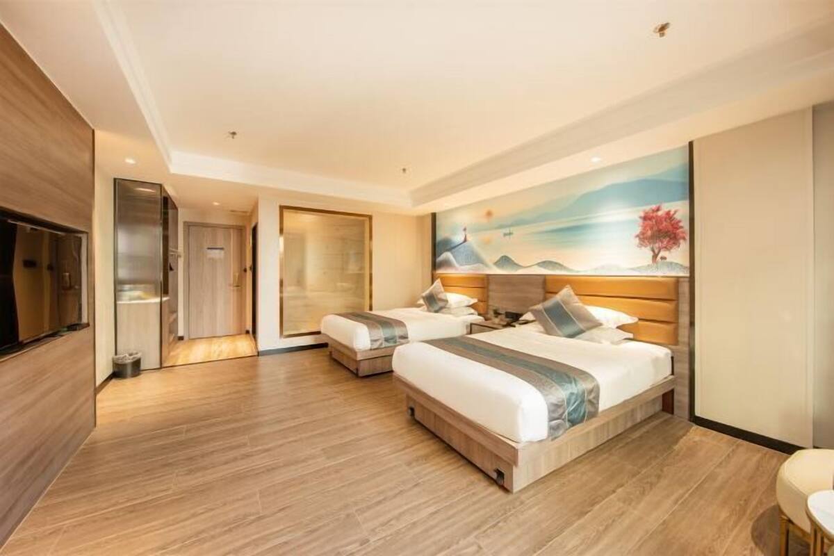 A hotel room with two beds, a TV, a painting, and a wooden floor.