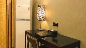 Quarto de hotel com escrivaninha de madeira, uma cadeira, abajur e geladeira.