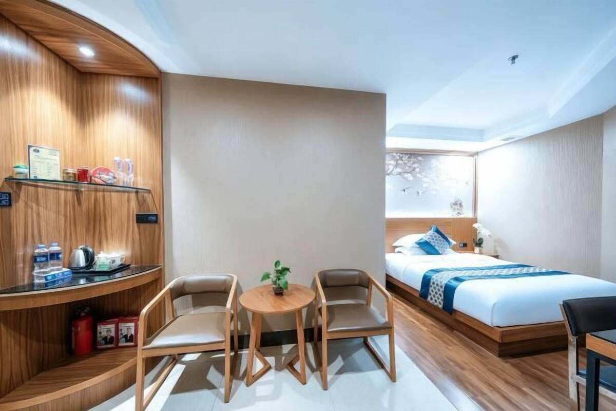 A hotel room with a wooden desk, two chairs, a bed, and a small table with a plant.