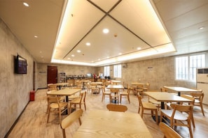 A spacious dining area with multiple tables and chairs, a high ceiling with recessed lighting, and a view of the kitchen area. - Jiangmen Park Lane Hotel (Gangzhou Avenue Baiyi Branch) (Jiangmen)