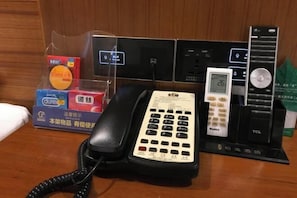 A hotel room with a desk, a telephone, a digital clock, and a charging station.