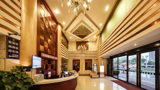 Um saguão de hotel com um balcão de recepção, um candelabro e uma grande janela com vista para a rua.
