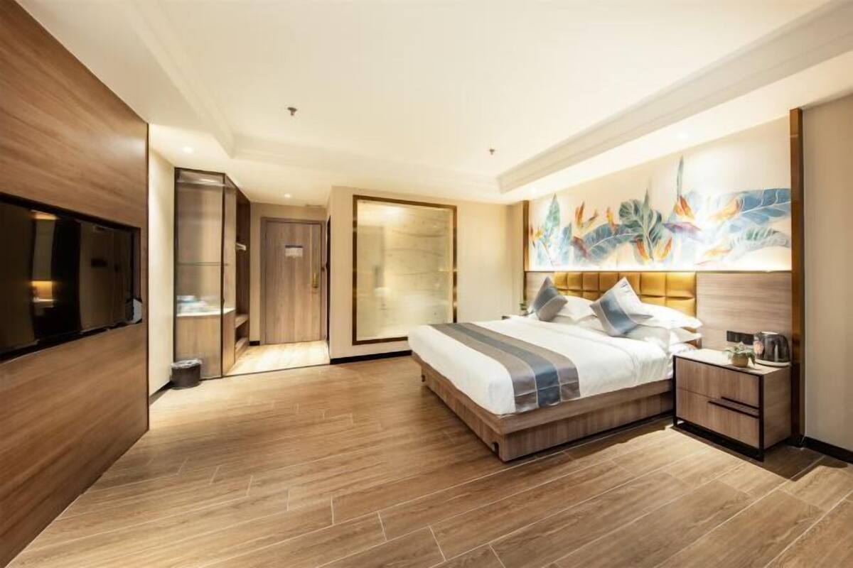 A modern hotel room with a large bed, a bedside table, a TV, and a bathroom with a glass door.