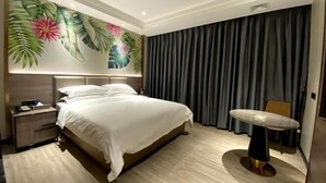 Quarto de hotel com uma cama grande, uma mesa de cabeceira, uma mesinha e um mural na parede.