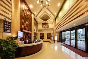 A hotel reception area with a curved reception desk, a chandelier, and a large window offering a view of the city. - Jiangmen Park Lane Hotel (Gangzhou Avenue Baiyi Branch) (Jiangmen)