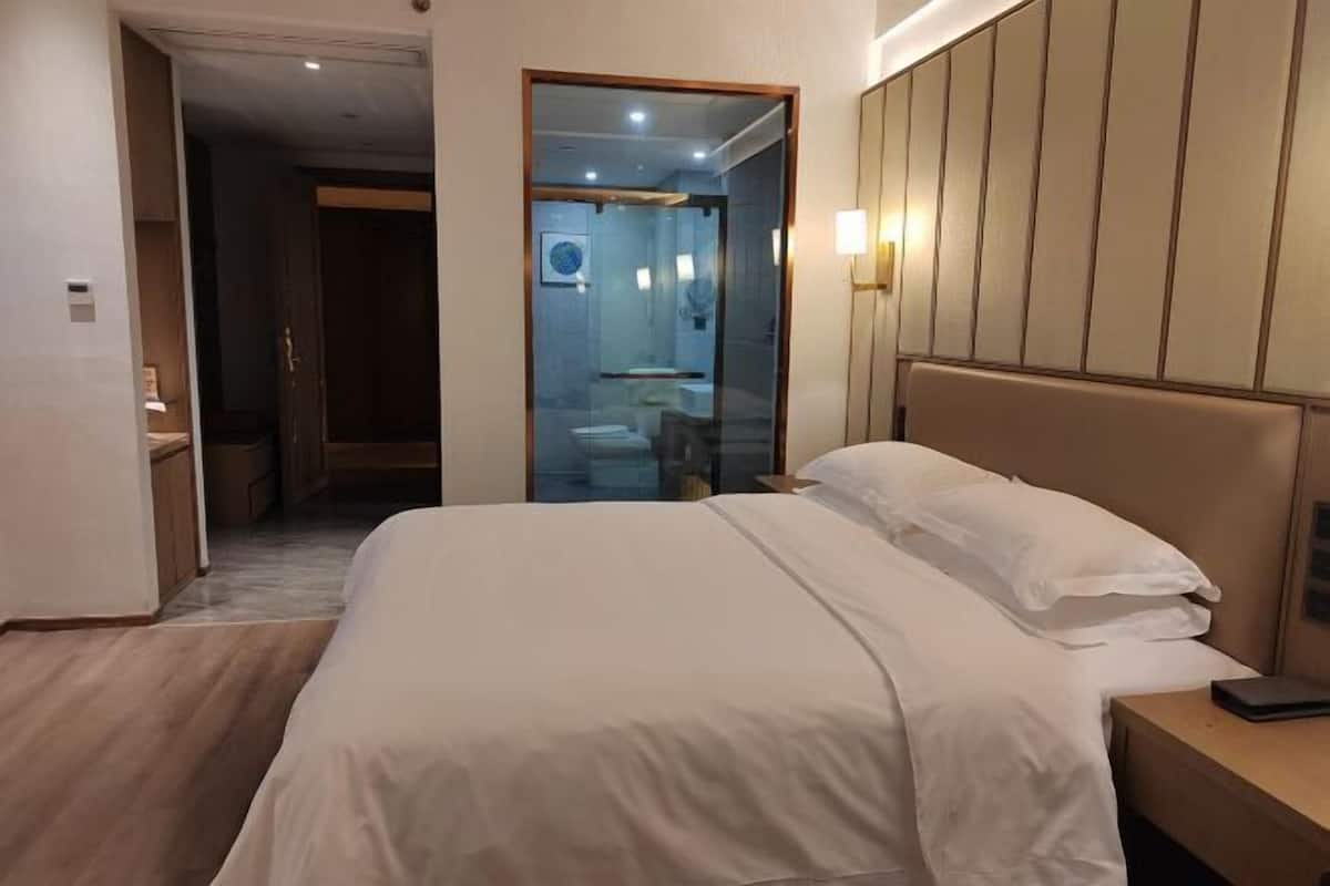 Une chambre d’hôtel comprenant un lit, une table de chevet et une douche séparée par des parois en verre.