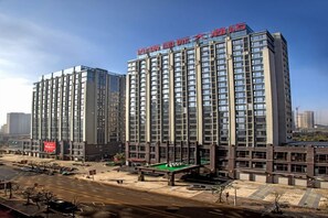 A high-rise hotel with multiple floors, a parking area, and a green space with a pool table.