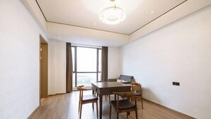 Ein modernes Zimmer mit Holzboden, einem Esstisch mit Stühlen, einer Couch und einem großen Fenster mit Vorhängen.