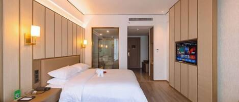 A hotel room with a bed, bedside table, lamp, TV, and a view of the hallway.