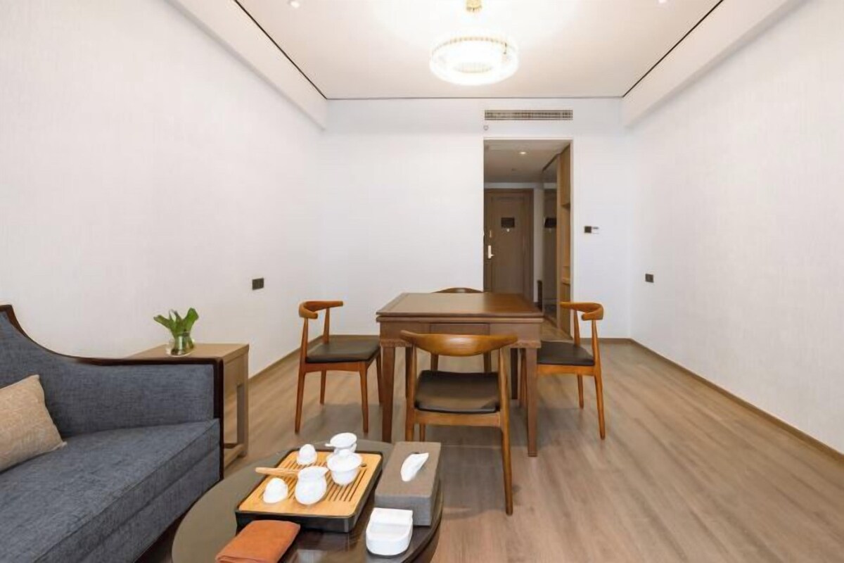 A modern living room with a sofa, dining table, and chairs. There is a small side table with a plant and a tray of tea utensils.