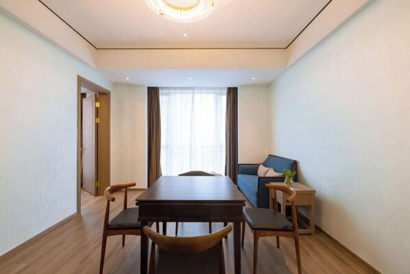 A modern hotel room with a dining table, chairs, a sofa, and a small side table with a plant.