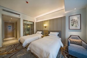 A hotel room with two beds, a seating area, and a framed artwork on the wall.