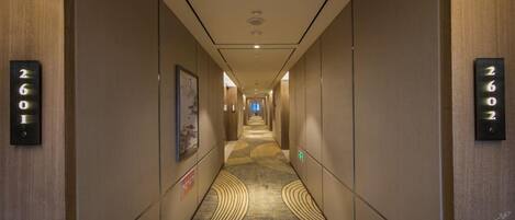 Un pasillo de hotel con piso alfombrado, números de habitaciones en la pared y un cuadro enmarcado.