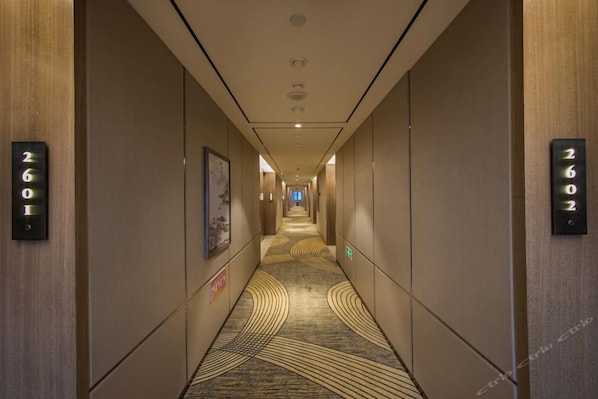 A hotel hallway with a carpeted floor, wall-mounted room numbers, and a framed picture.