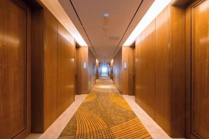 Un couloir d’hôtel avec des portes en bois de chaque côté et un tapis à motifs.