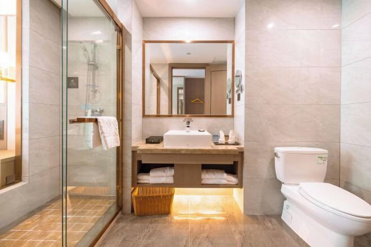 Une salle de bain moderne avec une douche à l’italienne en verre, un lavabo avec un miroir au-dessus et des toilettes.