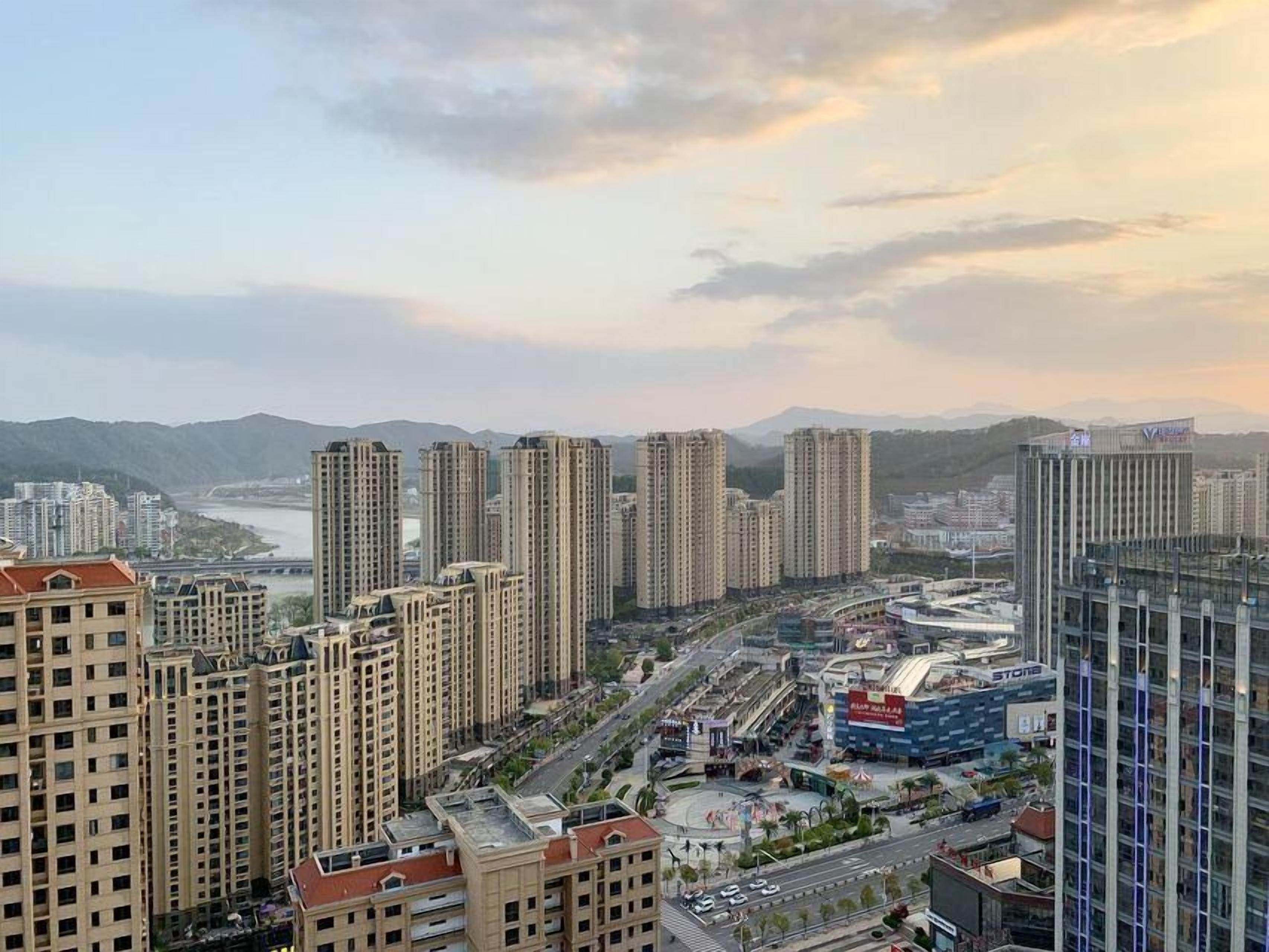 A high-rise residential building complex with multiple apartment buildings, a central plaza, and a river in the background.