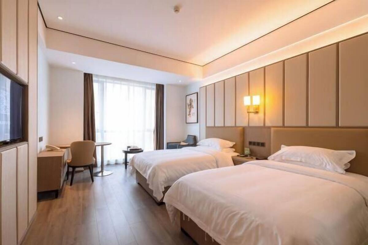 Une chambre d’hôtel avec deux lits, un bureau, une chaise et une fenêtre avec des rideaux.
